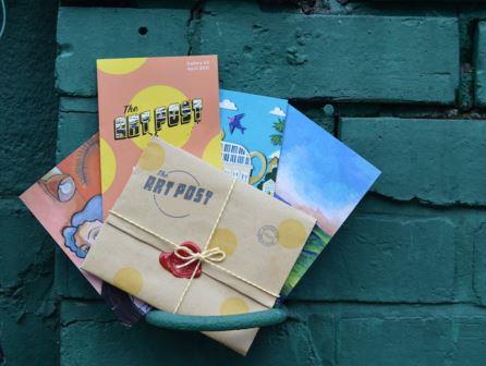 Photo of a mail out from the Art Post Sheffield, showing 3 high quality art cards, the artists' stories and hand sealed wrapping against a brick wall