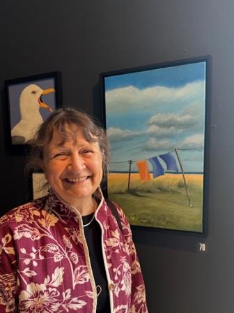 Judy Randle infront of a brightly coloured acrylic painting of a washing line with towels fluttering in the wind.
